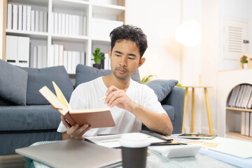 A man is sitting on the floor. He is looking at his credit card and checking his expenses on his...
