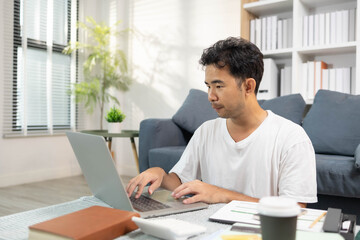A man is sitting on the floor. He is looking at his credit card and checking his expenses on his...