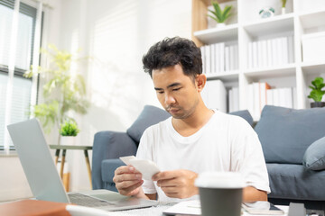 A man is sitting on the floor. He is looking at his credit card and checking his expenses on his...