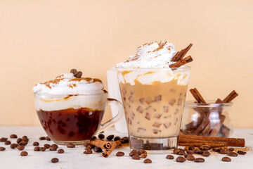 Iced cinnamon latte with whipped cream, cinnamon syrup and cinnamon powder on top, with coffee beans on white and beige background copy space