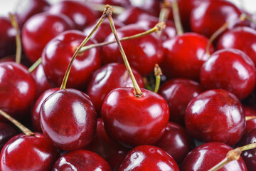 Vibrant closeup, macro of organic fresh ripe sweet cherries with stems, arranged in a natural pile. The deep red color, glossy texture, and fresh look. Food background, wallpaper, backdrop
