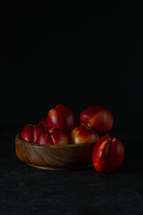 peaches lie in a wooden bowl on a dark background
