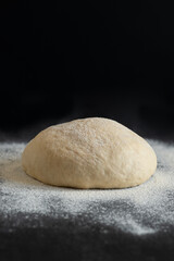 Close-up shot of dough lying on a dark table. There is a bottle of oil in the back. Flour is pouring.