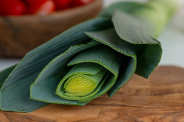 Close-up shot of a onion lettuce lying on a wooden texture cutting board. . In the background are tomatoes in a wooden-textured bowl