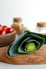 Close-up shot of a onion lettuce lying on a wooden texture cutting board. . In the background are tomatoes in a wooden-textured bowl and glass jars of spices.