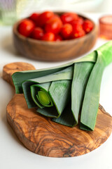 Close-up of a onion lettuce lying on a wooden texture cutting board. . In the background are tomatoes in a wooden-textured bowl and glass jars of spices.