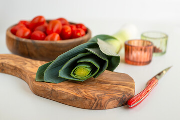 wooden texture cutting board. Nearby lies a knife with a red stylish handle. In the background are tomatoes in a wooden-textured bowl and glass jars of spices.