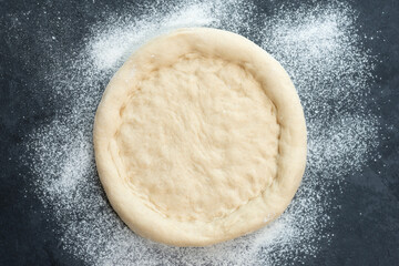 Close-up of a workpiece of pizza dough lying on a dark table