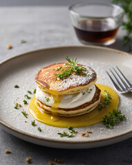 A plate of fluffy pancakes topped with creamy sauce and fresh herbs