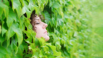 A young woman with curly hair and facial piercings nestles her face peacefully into a dense wall of...