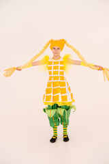 Cheerful girl having fun, dancing and laughing on light background in yellow corn costume with funny facial expression in empty space. vertical.