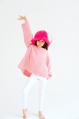 Excited girl model in pink hat posing in studio. Clothes, children's fashion concept. Positive child dancing in studio. vertical