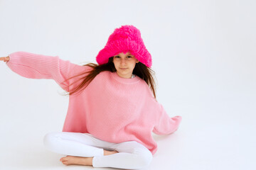 Excited girl model in pink hat posing in studio. Clothes, children's fashion concept. Positive child dancing in studio