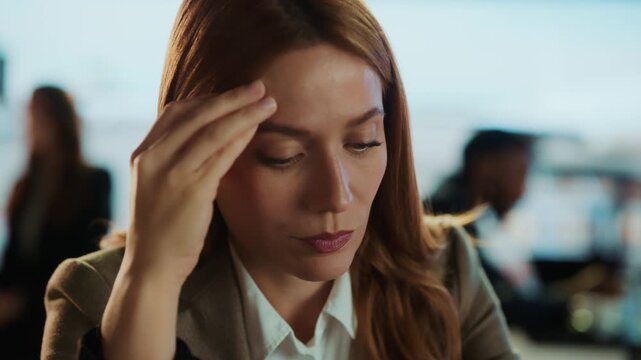 A concerned businesswoman touches her eye in a pensive moment. The interior setting and the soft focus enhance the reflective mood.