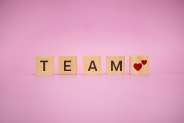 TEAM word formed with wooden blocks and heart symbols on pink background