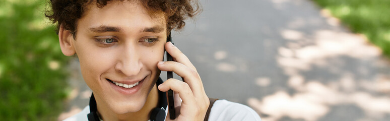 Curly haired young man enjoying a sunny day at the park while chatting on the phone