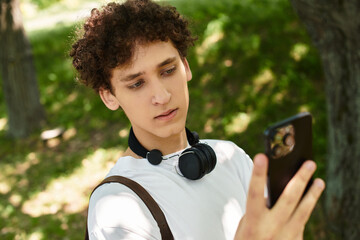 Young man with curly hair relaxes in a green park, checking his phone