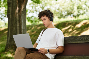 Young man enjoys casual afternoon in green park while working on laptop