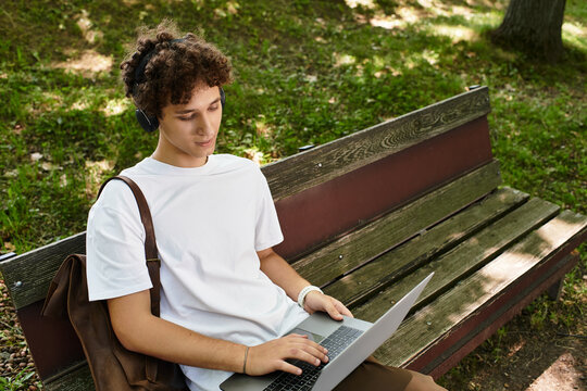 Curly-haired young man enjoys a relaxing day in the park while working on his laptop