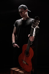 A musician stands confidently with a guitar in a dark environment, showcasing his artistic...