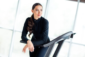 Young woman in activewear leaning on a treadmill during workout in a bright gym with natural...