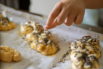 A child's hand sprinkles toppings on the dough for baking sweet buns. Baking master class