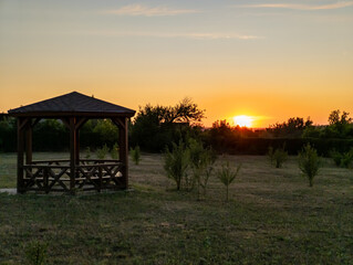 A gazebo in the middle of a grassy field with a sunset in the background