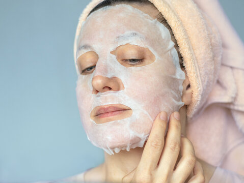 Woman applying a fabric cosmetic mask to her face to care for her skin at home