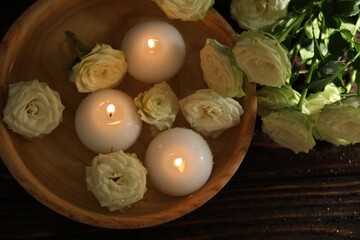 Burning candles, water and rose flowers in bowl on wooden table, flat lay