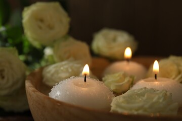 Burning candles, water and rose flowers in bowl on wooden table, closeup