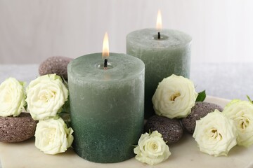 Burning candles, stones and rose flowers on table, closeup
