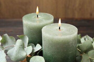 Burning candles and eucalyptus branches on wooden table, closeup
