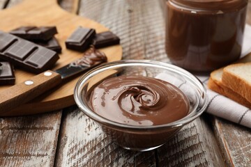 Tasty chocolate butter in glass bowl on color wooden table, closeup