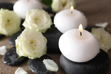 Burning candles, stones and rose flowers on wooden table, closeup