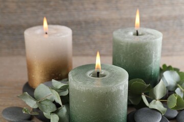 Burning candles, stones and eucalyptus branches on wooden table, closeup