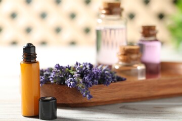 Bottles of essential oil and flowers on white wooden table, closeup
