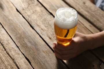 Man with glass of beer at wooden table, closeup. Space for text