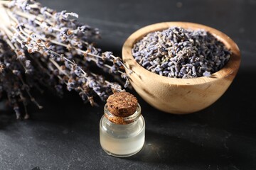 Natural essential oil and lavender flowers on black table, closeup