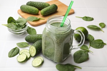 Tasty smoothie in mason jar, spinach leaves and cucumber on white tiled table, closeup