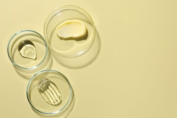 Different cosmetic products in Petri dishes on pale yellow background, flat lay. Space for text