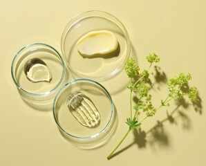 Different cosmetic products in Petri dishes and floral decor on pale yellow background, flat lay