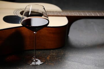 Acoustic guitar and red wine on black table, closeup