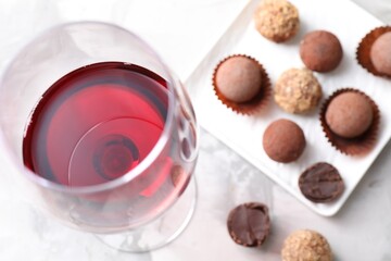 Red wine in glass and truffle bonbons on light table, above view