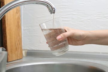 Woman filling glass with dirty tap water indoors, closeup