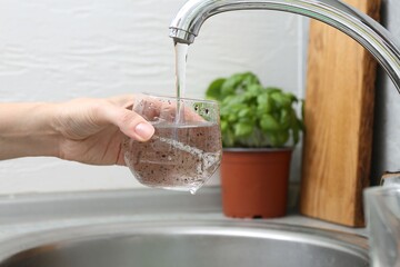 Woman filling glass with dirty tap water indoors, closeup