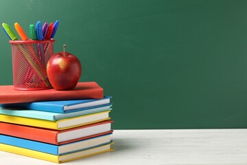 Different school stationery and red apple on white wooden table against blackboard, space for text
