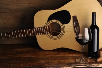 Acoustic guitar, bottle and glass of red wine on wooden table