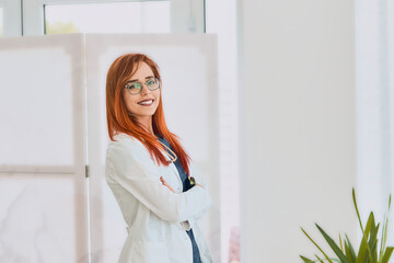 Portrait of confident smiling female doctor with arms crossed, looking at the camera in modern...