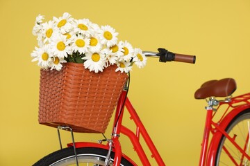 Bicycle with basket of beautiful flowers on yellow background, closeup