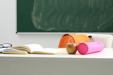 Different school stationery, glasses and apple on white table near blackboard indoors